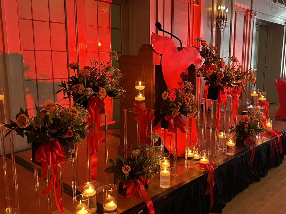 Photo of red dress cutout in front of podium surrounded by red flowers and candles.